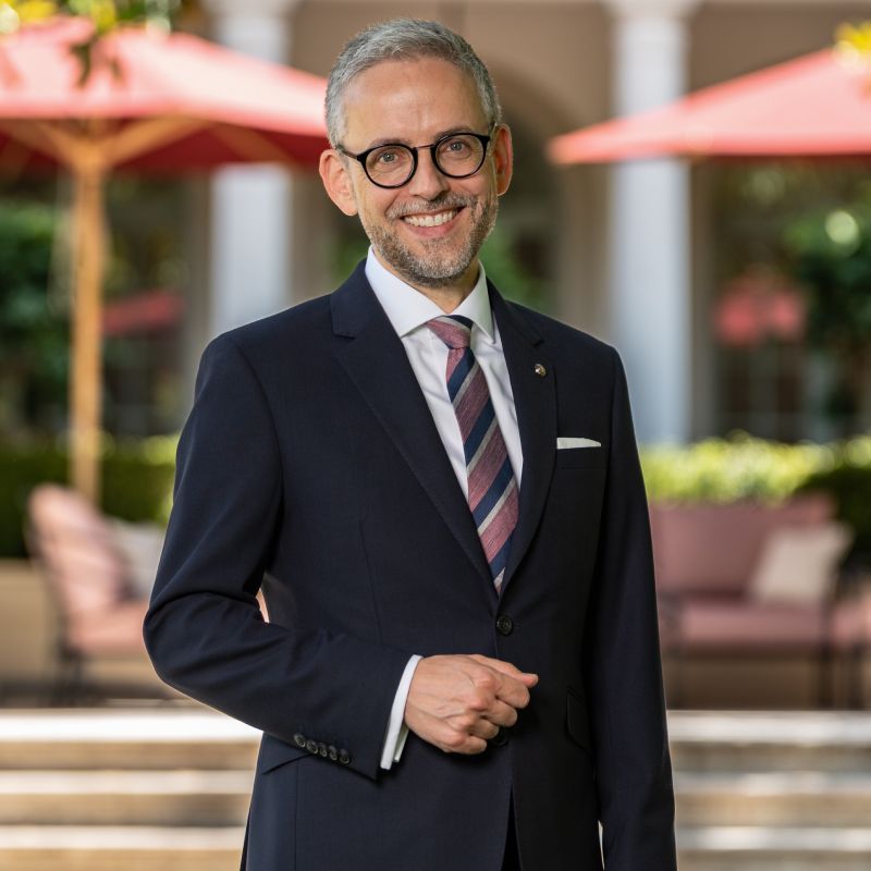 Man in suit with glasses smiling outdoors under umbrellas