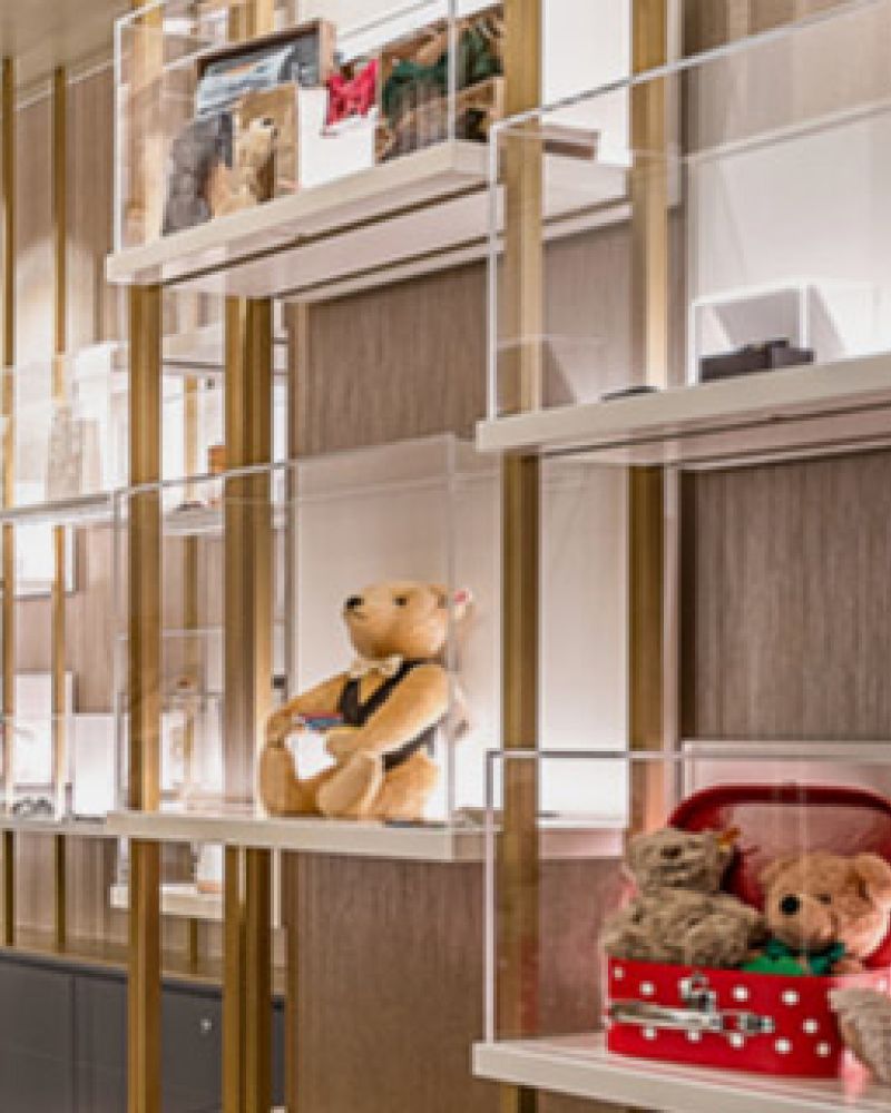 Display shelf with teddy bears in suit, suitcase, on wood-textured background