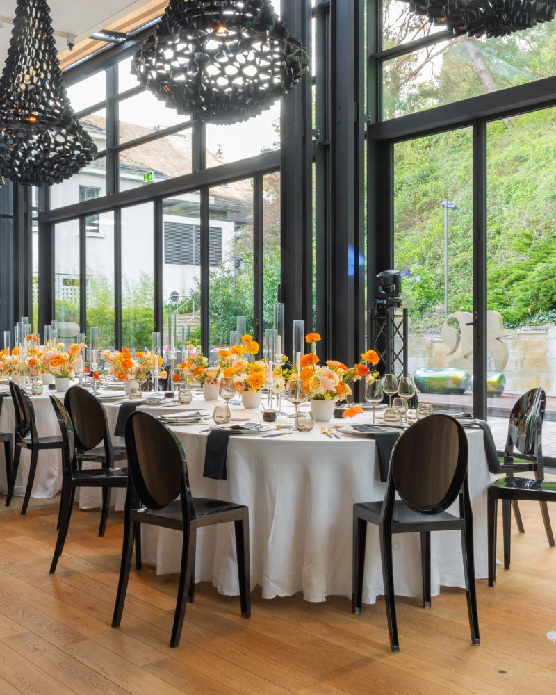 Modern dining setting with white tablecloth, orange flowers, and tableware
