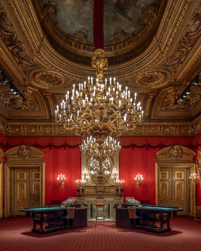 Opulent room with chandelier, red walls, gold accents, and gaming tables.