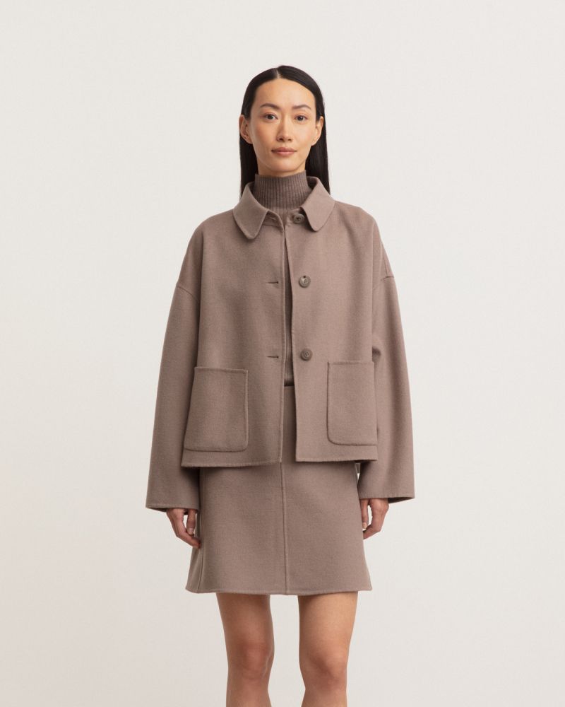 Woman in light brown outfit with jacket and skirt against plain background