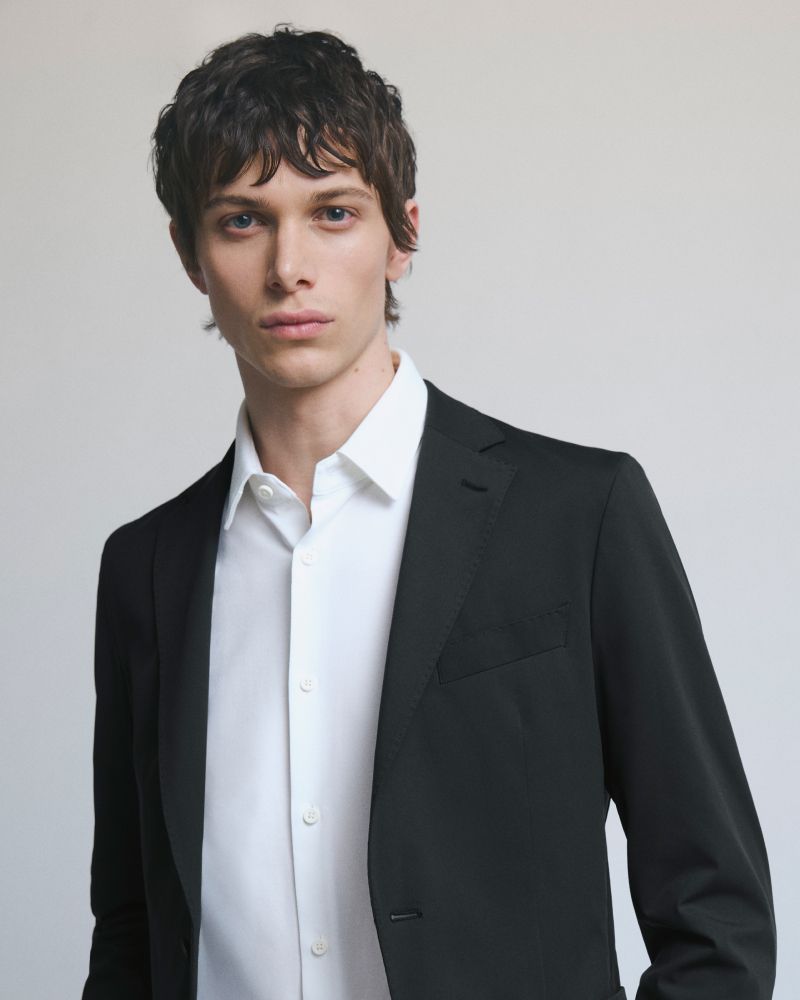 Young man in black suit with serious expression on neutral background