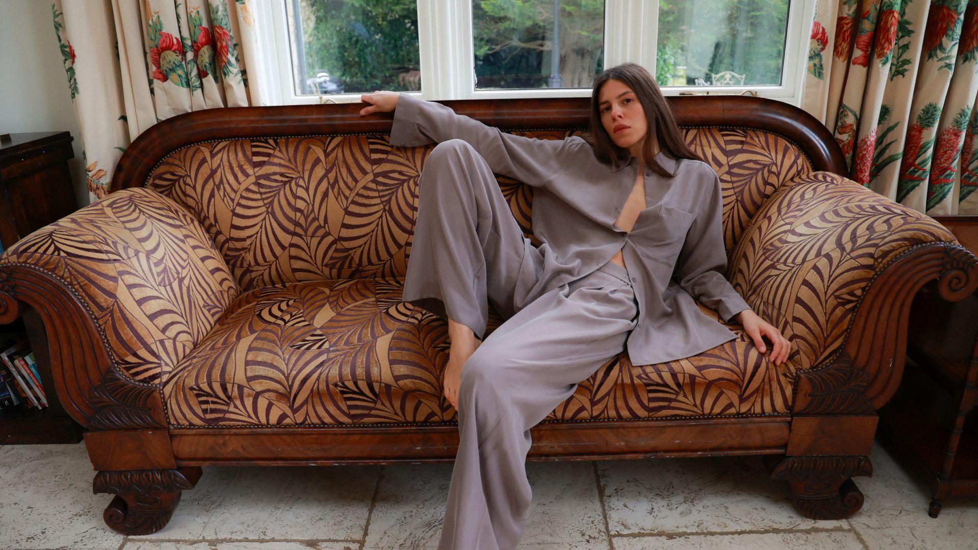 Person in light outfit on ornate leaf-patterned couch with natural light from windows
